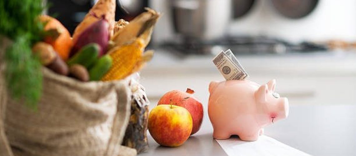 Closeup on money in piggy bank and purchases from local market on table