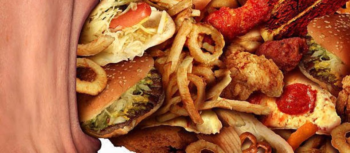 Eating junk food nutrition and dietary health problem concept as a person with a big wide open mouth feasting on an excessive huge group of unhealthy fast food and snacks.